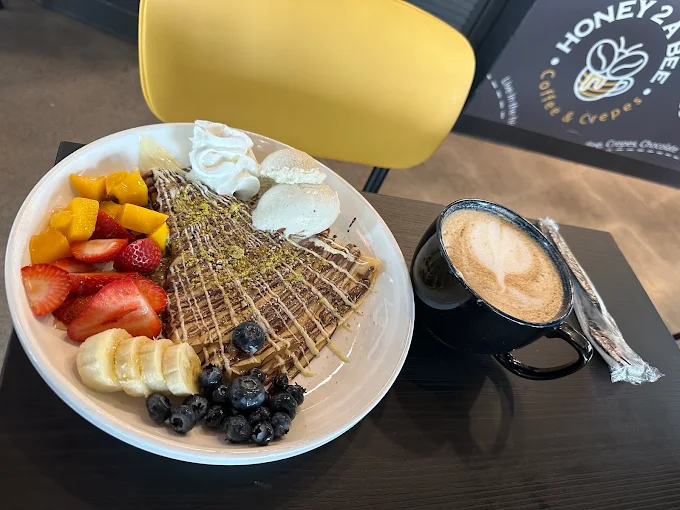 A crepe with fresh fruit and whipped cream next to a latte on the table at Honey2ABee in Tempe, Arizona